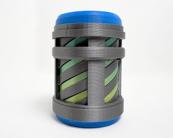 May include: A cylindrical object featuring a bright blue top and bottom cap. The central section consists of a dark gray cage structure with vertical and horizontal bands, revealing diagonal light green and dark gray stripes underneath.
