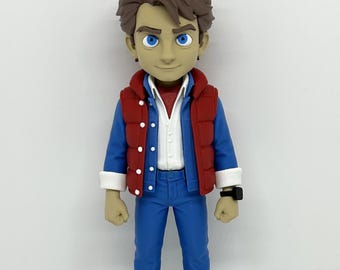 May include: A stylized collectible figure of a character with brown hair and blue eyes, wearing a red puffer vest over a blue denim jacket, white shirt, blue jeans, and white sneakers with black accents. The text NOXMS is visible in the top right corner.