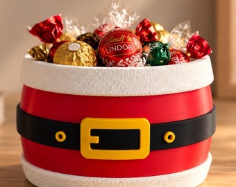 May include: A cylindrical red container with a white textured rim at the top and bottom, featuring a black belt design with a yellow buckle and two yellow studs. The container is filled with assorted Lindt Lindor chocolate truffles.