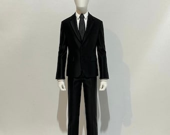 May include: A white faceless mannequin wearing a black suit, a white collared shirt, and a dark patterned tie. The figure stands upright with arms at its sides. The text NOXMS is printed in black and red in the upper right corner.