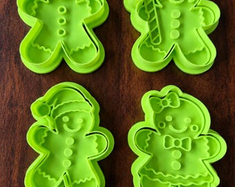 May include: A set of four bright lime green plastic cookie cutters shaped like gingerbread figures. One figure is plain, one holds a candy cane, one wears a Santa hat, and one features a bow on the head and a bow tie on the chest.