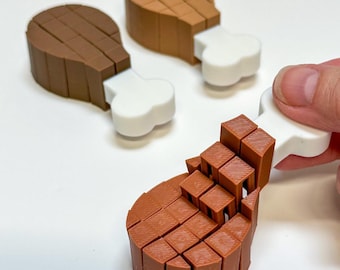 May include: Three chicken leg-shaped objects made of brown and white plastic. Each piece features a brown, blocky, grid-like texture representing meat and a smooth, white, bone-shaped handle. One piece is held, while two others rest nearby.