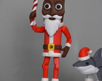 May include: A brown-skinned Santa Claus action figure wearing a red suit with white trim, a belt with a yellow buckle, and a red hat, holding a red and white striped candy cane. Beside it stands a gray shark figure wearing a red Santa hat.