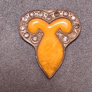 May include: Vintage brooch with a heart-shaped design. The brooch features a central yellow enamel shape, surrounded by a silver-toned metal frame. The frame is embellished with clear, sparkling rhinestones, adding a touch of elegance to the piece.