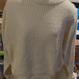 Könnte beinhalten: Cremefarbener Pullover mit gerippter Strickstruktur. Der Pullover hat einen Rundhalsausschnitt und lange Ärmel. Der Saum und die Manschetten sind ebenfalls gerippt. Der Pullover wird auf einer Schaufensterpuppe präsentiert.