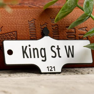 May include: White metal street sign with black lettering that reads "King St W" and the number "121".
