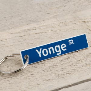 May include: A blue and white keyring with a silver ring. The keyring has the text "Yonge St" on it.