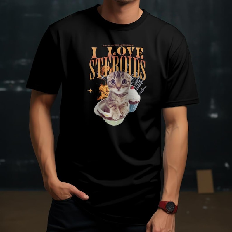 Puede incluir: Camiseta negra con un gr&aacute;fico de un gatito en un taz&oacute;n con una magdalena y el texto "I LOVE STEROIDS".