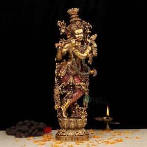 Op de afbeelding: Een gedetailleerd messing beeld van een godheid die fluit speelt. De figuur is versierd met ingewikkelde sieraden en kleurrijke accenten. Het beeld staat op een decoratieve basis, met een donkere achtergrond.