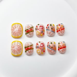 Peut inclure: Ensemble de dix faux ongles avec un motif de citron et d'agrumes. Les ongles sont peints avec une base rose clair et présentent divers motifs, notamment des citrons, des limes et des tranches d'orange. Certains ongles ont un motif de rayures vertes et rouges.