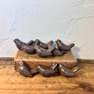 May include: A collection of seven small, dark brown, bird-shaped figurines with a glossy finish. Four of the bird figures are arranged on top of a rectangular wooden box, while three additional bird figures are positioned in front of the box.