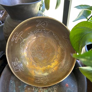 May include: A brass bowl with intricate engravings of Chinese characters and floral designs. The bowl is a traditional Chinese design and is perfect for serving tea or other beverages.