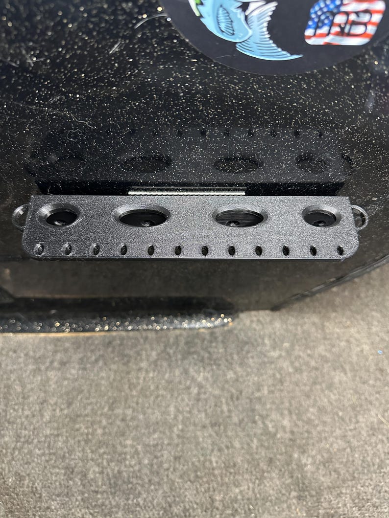 May include: Black metal rod with five round holes and a row of smaller holes. The rod is mounted on a black surface.
