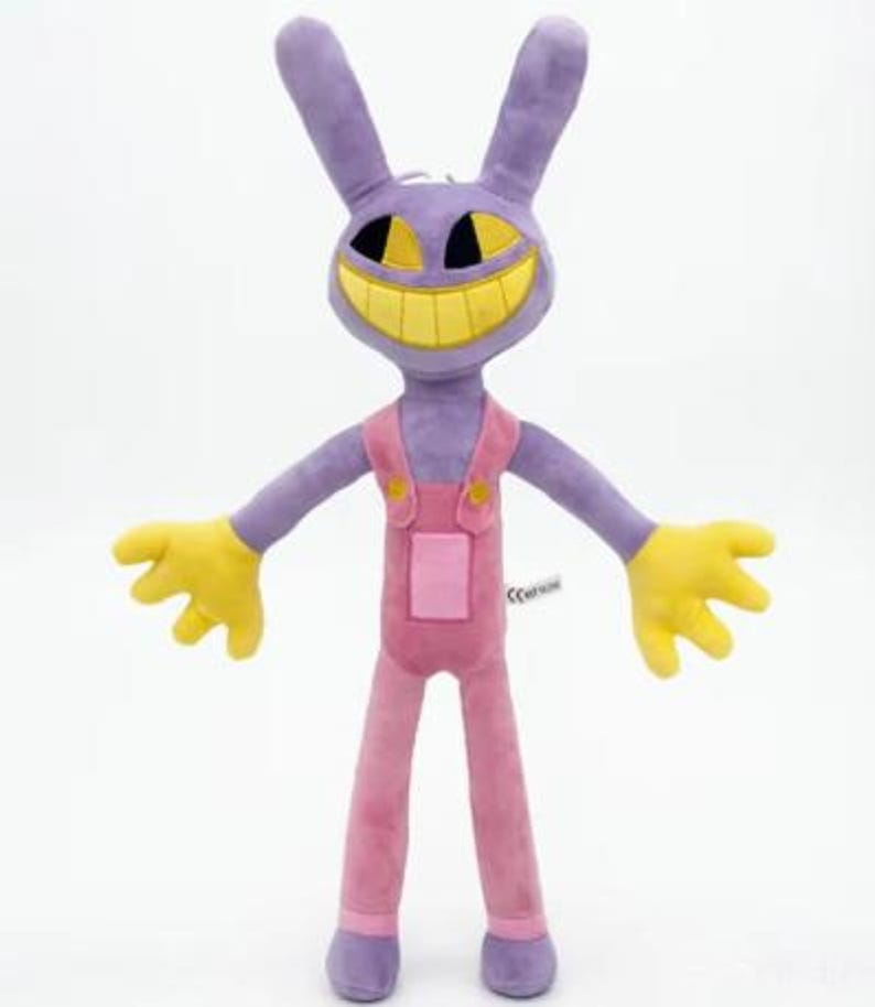 May include: A plush toy shaped like a purple rabbit with long ears, yellow hands, and a wide yellow grin. The character wears pink overalls with yellow buttons and a small square pocket on the front. The fabric has a soft, smooth texture throughout.