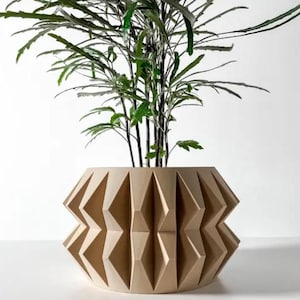 Può includere: Un vaso da fiori geometrico beige con una pianta con foglie verdi. Il vaso è in legno e ha un design unico ispirato all'origami.