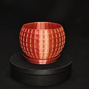 May include: A red, spherical planter with a grid pattern. The planter has a small base and is made of a smooth, plastic-like material.