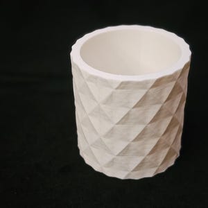 Puede incluir: Maceta de cerámica blanca con un patrón geométrico de diamantes. La maceta es cilíndrica y tiene un interior blanco liso.