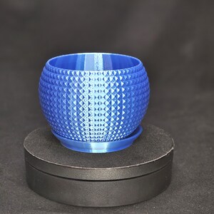 May include: A blue, spherical planter with a diamond pattern. The planter sits on a matching blue saucer. The planter is approximately 4 inches in diameter and is suitable for small plants or succulents.