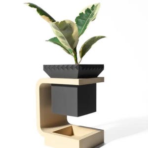 Puede incluir: Un soporte para plantas negro y beige con una maceta negra. La maceta tiene un patrón geométrico y contiene una planta verde con hojas variegadas.