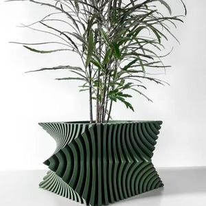 Op de afbeelding: Een donkergroene plantenpot met een geometrisch, golvend ontwerp. De pot is gevuld met een groene, bladerrijke plant.