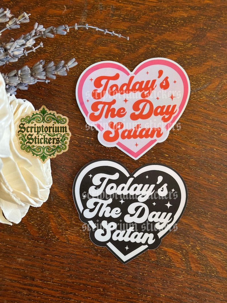 May include: Two heart-shaped stickers featuring the text Today's The Day Satan in a retro font. One sticker has a white background with a pink border and red text, while the other has a black background with a white border and white text.