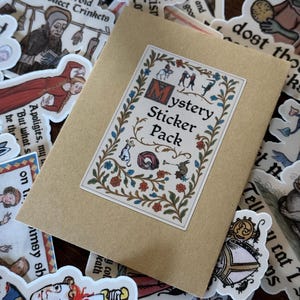 Pode incluir: Um envelope de papel bege com a etiqueta "Mystery Sticker Pack" e um autocolante decorativo com ilustra&ccedil;&otilde;es em estilo medieval. O envelope &eacute; rodeado por v&aacute;rios autocolantes com tema medieval.