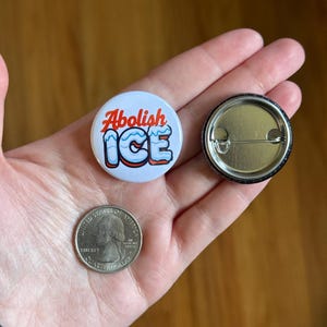 May include: A white button with the text "Abolish ICE" in red and blue. The button is next to a quarter coin and a button back.