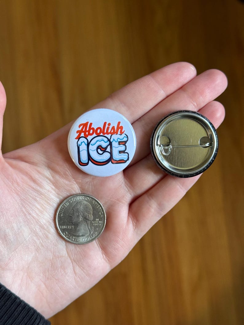 May include: A white button with the text "Abolish ICE" in red and blue. The button is next to a quarter coin and a button back.