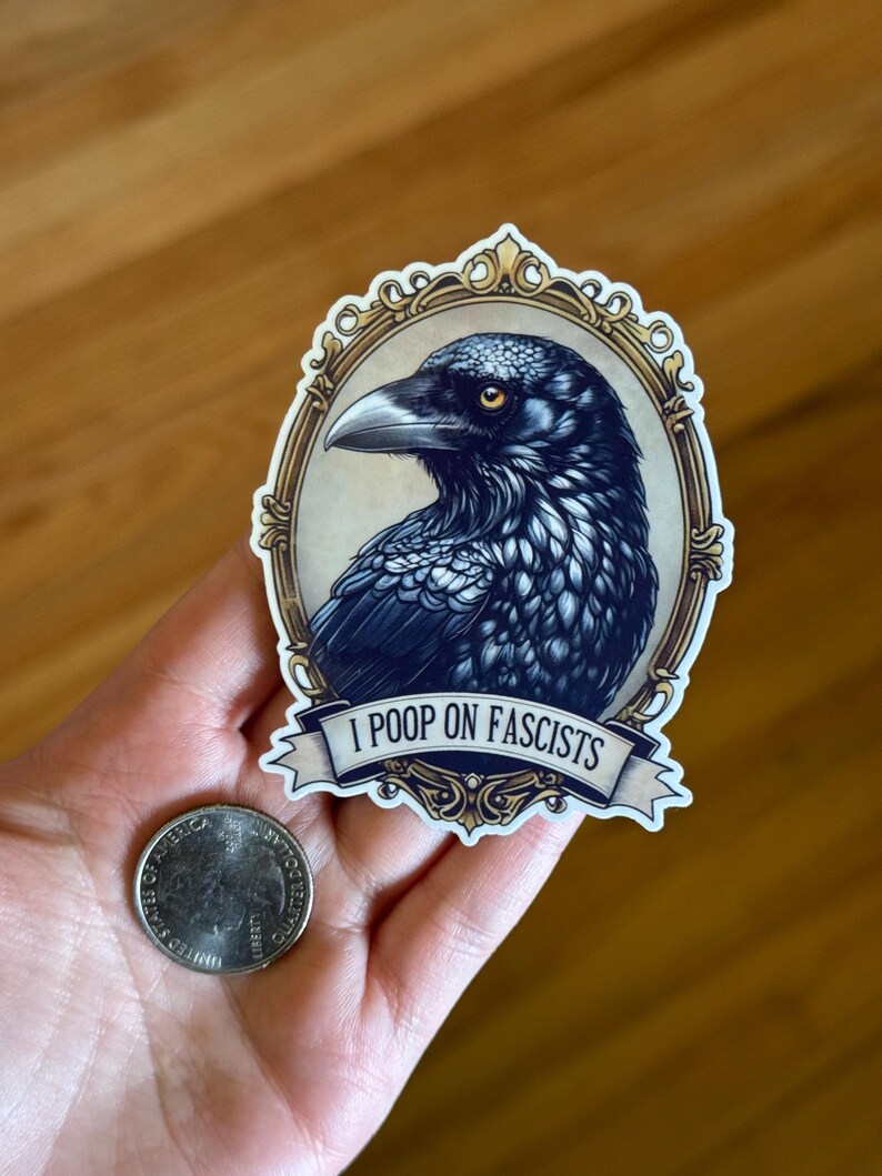 May include: A sticker with a detailed illustration of a raven in a gold frame. The raven is rendered in black and blue hues. A banner below the raven reads "I POOP ON FASCISTS".
