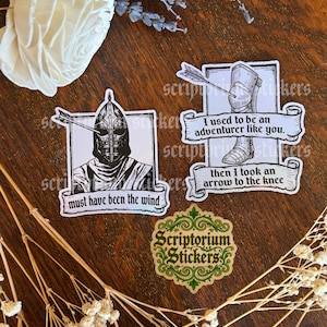 May include: A collection of stickers featuring medieval-themed designs. One sticker shows a knight with an arrow, text reads "must have been the wind." Another shows a leg with an arrow, text reads "I used to be an adventurer like you, then I took an arrow to the knee."