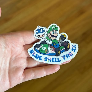 May include: A sticker featuring a cartoon image of Mario driving a kart with a blue shell. The text "Blue Shell the 1%" is written around the image.