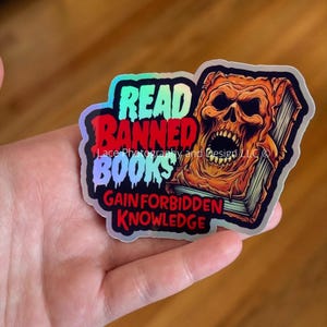 May include: Holographic sticker with the text "READ BANNED BOOKS GAIN FORBIDDEN KNOWLEDGE" and an illustration of a skull emerging from a book. The sticker has a black, red, and blue border.