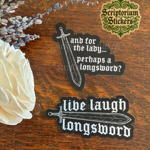 May include: Two black die-cut stickers with white text and sword illustrations. One sticker reads, "and for the lady... perhaps a longsword?" with a vertical sword. The other reads, "live laugh longsword" with a horizontal sword.