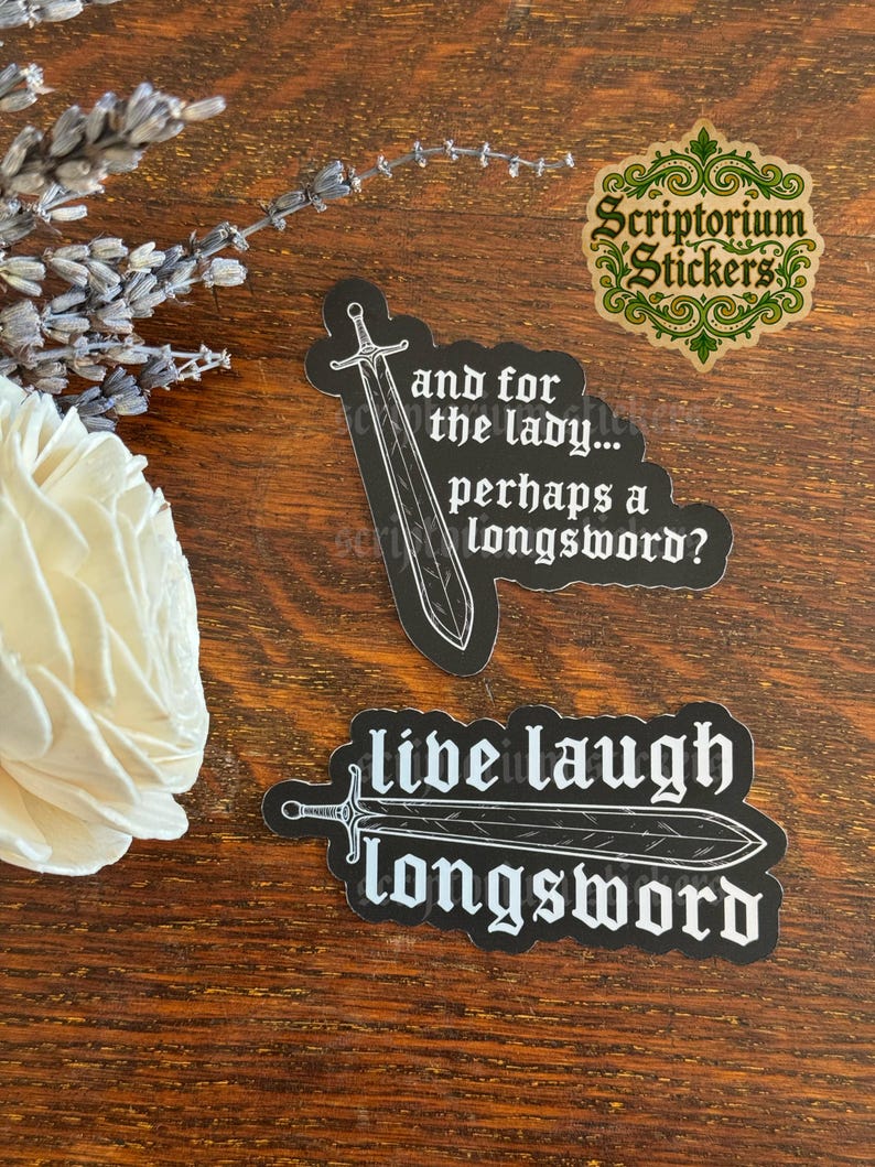 May include: Two black die-cut stickers with white text and sword illustrations. One sticker reads, "and for the lady... perhaps a longsword?" with a vertical sword. The other reads, "live laugh longsword" with a horizontal sword.