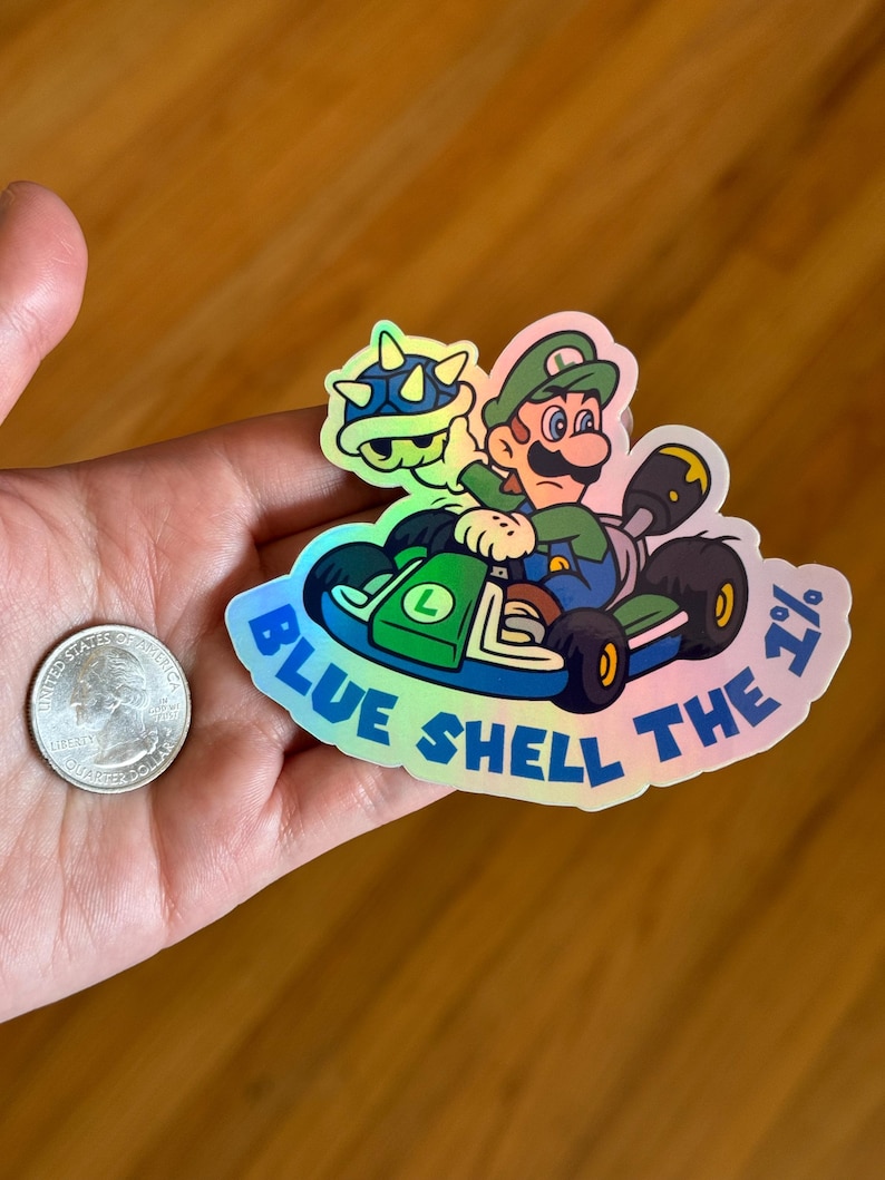 May include: A holographic sticker featuring a green cartoon character driving a kart with a blue shell. The text "Blue Shell the 1%" is written around the sticker.