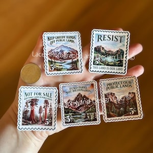 May include: A collection of rectangular stickers resembling vintage postage stamps. Each stamp features a landscape scene with text such as "Keep Greedy Hands Off Public Lands" and "Resist." The stamps are in various colors and include a 5-cent value.