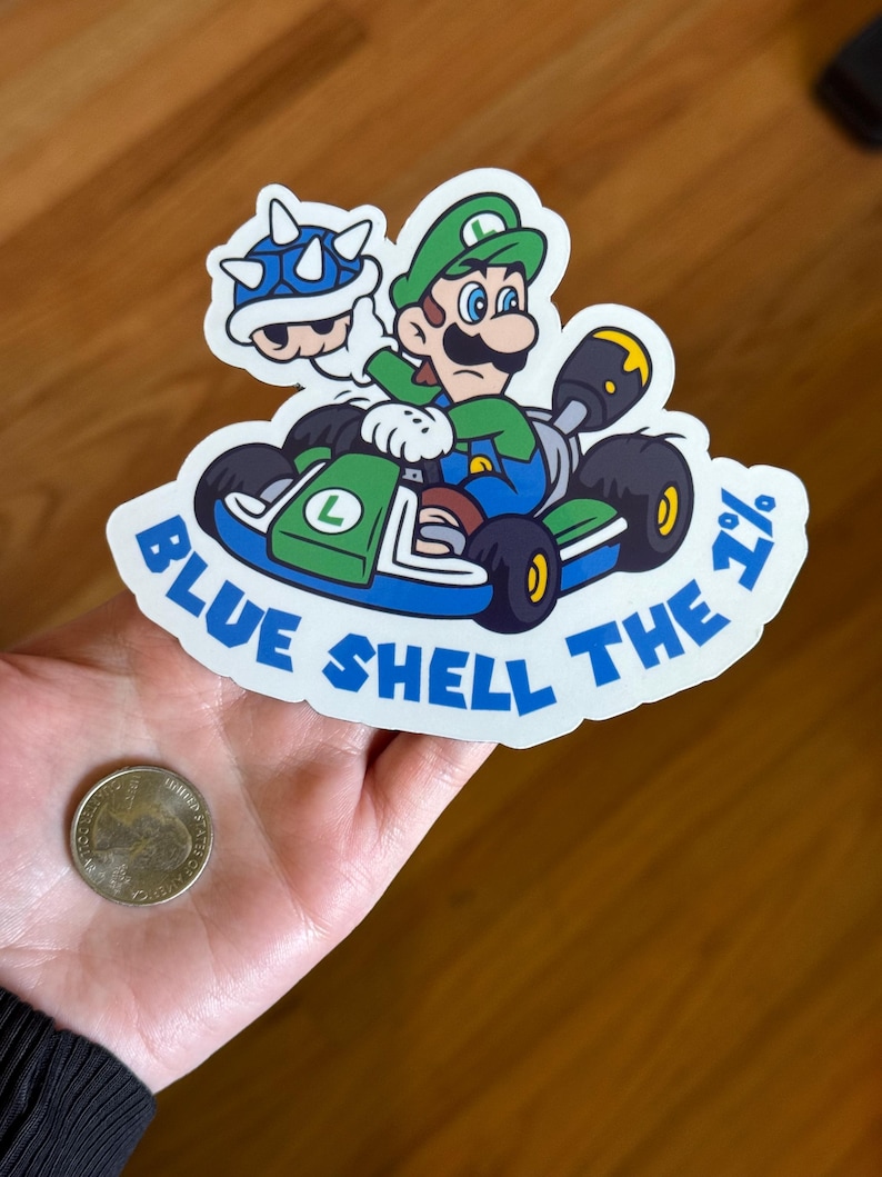 May include: A white sticker with a blue shell, green kart, and a green Mario character driving. The text on the sticker reads "Blue Shell The 1%".
