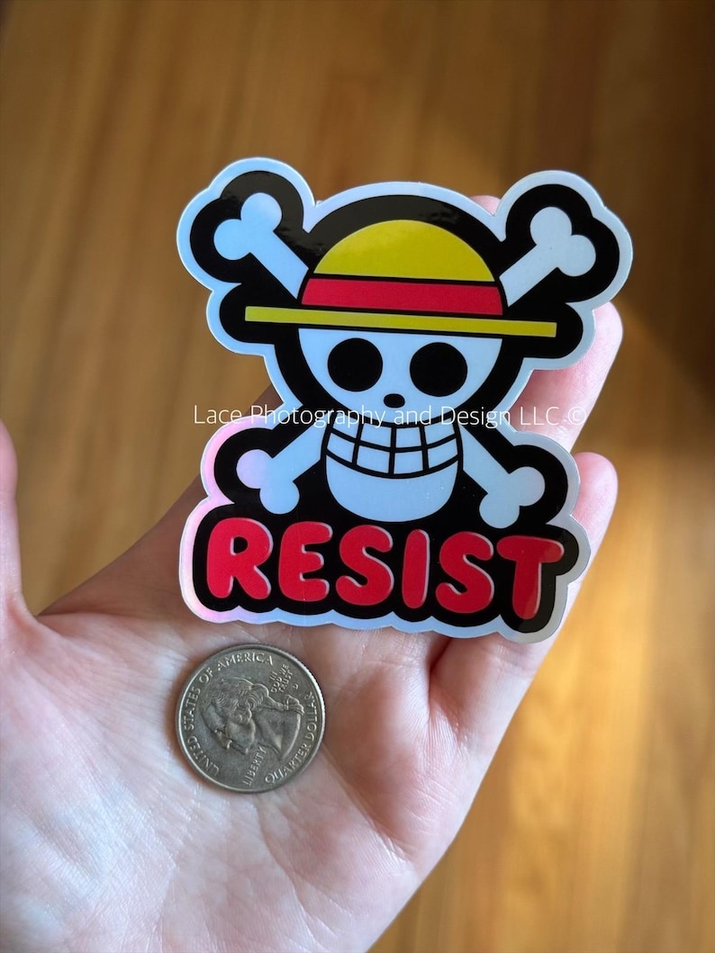 May include: A sticker featuring a skull and crossbones design with a yellow and red hat, and the word "RESIST" in red letters. A quarter coin is next to the sticker.