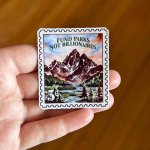 May include: A sticker resembling a vintage postage stamp, featuring a watercolor landscape of mountains, a river, and trees. The text "FUND PARKS NOT BILLIONAIRES" is at the top, with a "5&cent;" value in the corner.