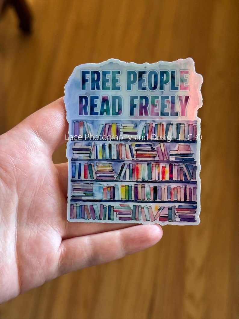 May include: A sticker with the text "FREE PEOPLE READ FREELY" above a watercolor illustration of a bookshelf filled with colorful books. The sticker has a watercolor effect with blue, purple, and pink hues.