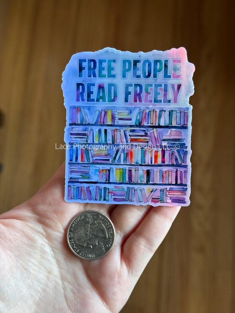 May include: A sticker with the text "FREE PEOPLE READ FREELY" above a watercolor illustration of a bookshelf. The sticker is held in a hand next to a quarter.