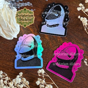 May include: Three stickers featuring a knight's helmet design. The stickers have a holographic effect, with colors shifting from blue to pink. The text "Scriptorium Stickers" is printed on the stickers.