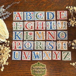 May include: A full alphabet of decorative stickers, each featuring a different letter in a colorful, ornate design. The letters are in various colors, including red, blue, green, and orange, with floral and scrollwork details. The stickers are arranged on a wooden surface.