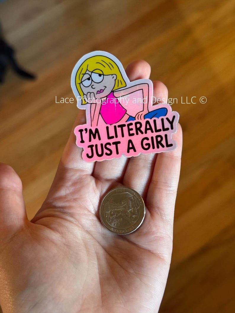 May include: A sticker featuring a cartoon girl with blonde hair and glasses, wearing a pink top and blue pants. The sticker has the text "I'M LITERALLY JUST A GIRL" in pink. A quarter is next to the sticker.