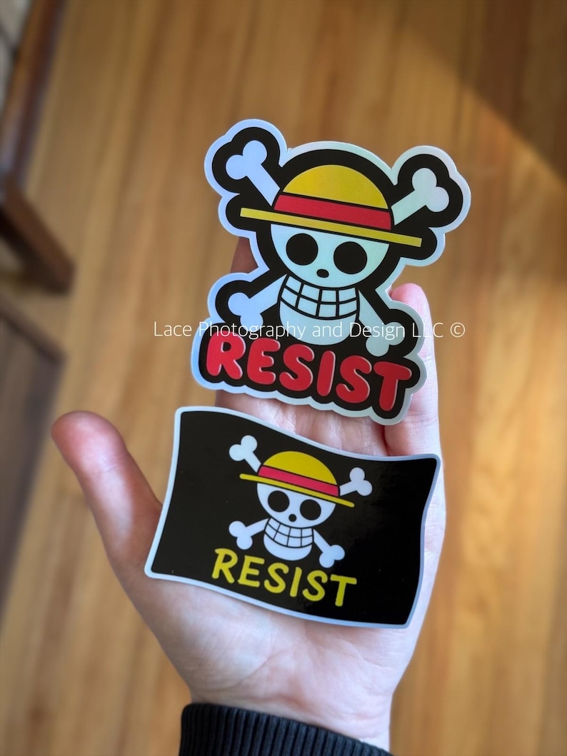 May include: Two stickers featuring a skull and crossbones design with a yellow hat and the word "RESIST". One sticker is a skull and crossbones with the word "RESIST" below it. The other sticker is a skull and crossbones with the word "RESIST" below it.