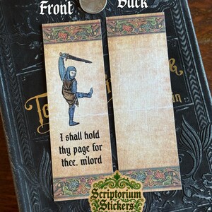 May include: A medieval-themed bookmark with a knight illustration on the front and blank space on the back. The front features a knight with a sword and the text "I shall hold thy page for thee, m'lord." The bookmark has decorative borders.