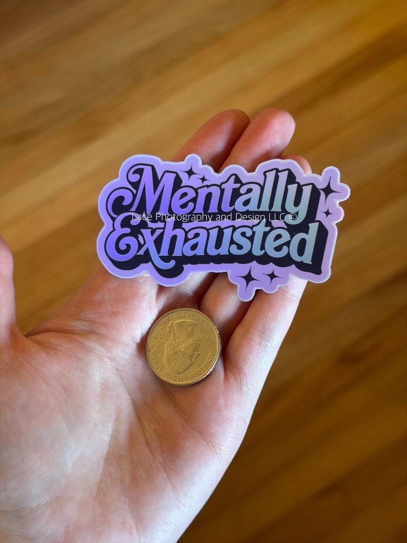 May include: A sticker with the words "Mentally Exhausted" in a purple and blue gradient design. The sticker has a decorative font and star accents. A gold coin is next to the sticker.