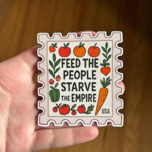 May include: A square sticker with a postage stamp design. The sticker features the text "FEED THE PEOPLE STARVE THE EMPIRE" with illustrations of vegetables and fruits. The sticker has a white border and the word "USA" at the bottom.