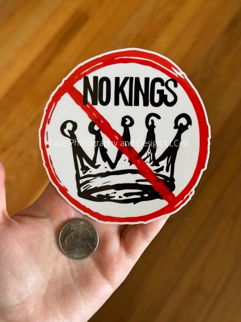 May include: A white sticker with a red circle and a red line through a black crown. The words "NO KINGS" are above the crown in black. A quarter is next to the sticker.