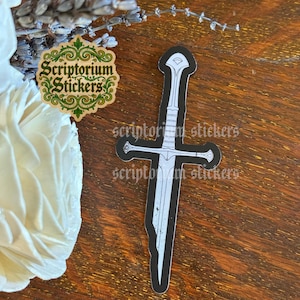 May include: A die-cut sticker featuring a black and white illustration of a broken sword with a pointed pommel and crossguard. The sticker has a black background and a white outline. The text Scriptorium Stickers is visible on the sticker.